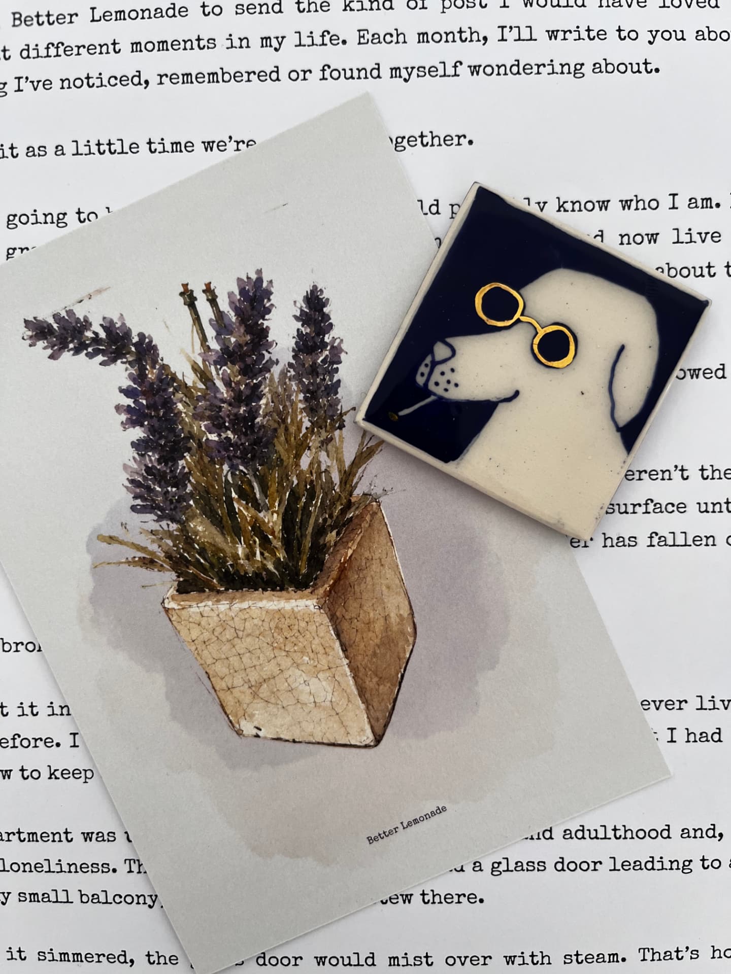 A lavender sprig card, a small ceramic dog with round glasses, and an envelope arranged on top of typewritten pages